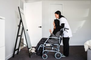 Caregiver assisting a smiling elderly woman in a wheelchair in front of a mirror, focusing on personal care tasks at home