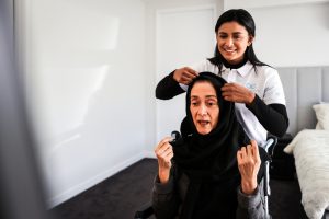 A support coordinator adjusts a scarf for a seated elderly woman, showing NDIS choice and control in home care.