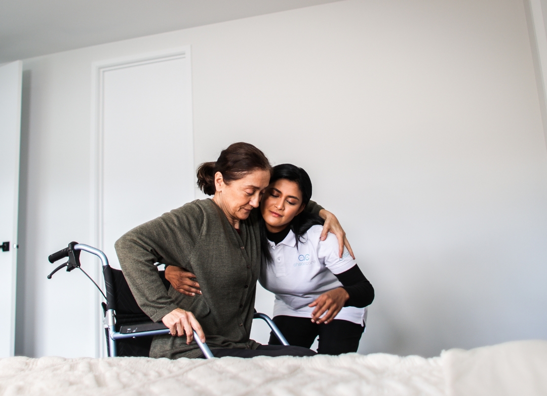 A woman in a wheelchair embraces another woman in a bed, symbolising support and care within NDIS services.