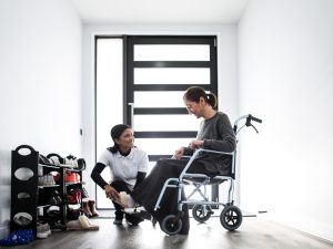 A caregiver helps a woman in a wheelchair near a door, highlighting NDIS transport assistance for improved mobility.