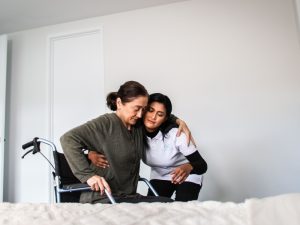 Healthcare worker providing assistance for disabled persons, helping an elderly woman transfer from a wheelchair to a bed.