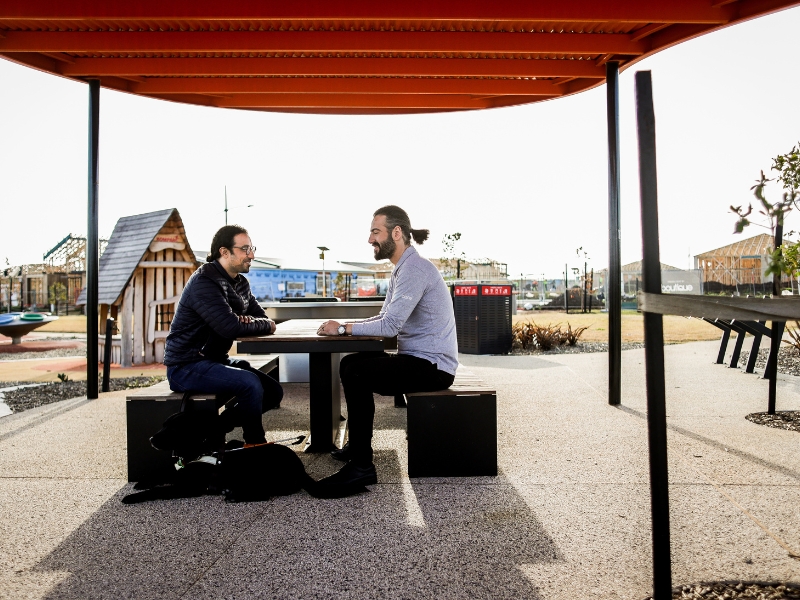 Two individuals talking at an outdoor table, showcasing innovative community participation in open and collaborative spaces.