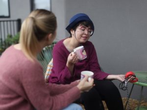 Two women having a casual conversation while holding mugs, discussing medication management in a relaxed setting.