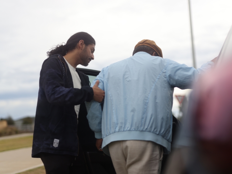 Young man assisting an elderly person into a car, highlighting accessible transport options.