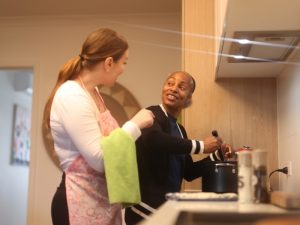 NDIS provider assisting an older woman in the kitchen with home assistant devices for safety and independence.