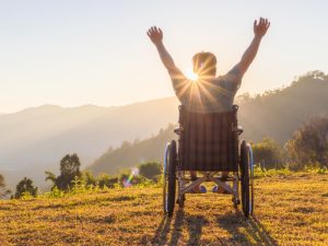 A man in a wheelchair raising his hands happily, highlighting the positive impact of travel assistance on accessibility.