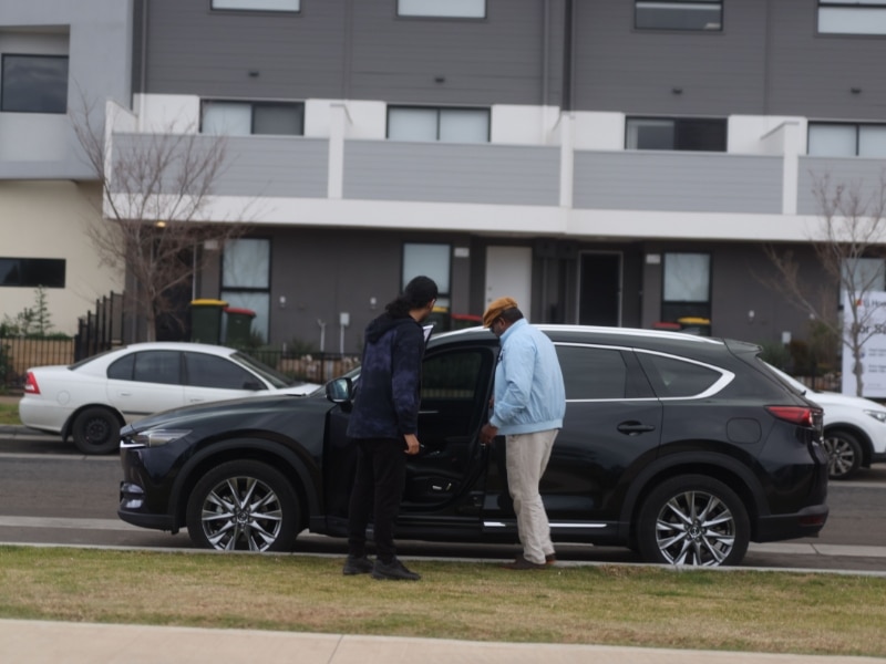 A man providing medical transport assistance, guiding a client to a car with care and support.