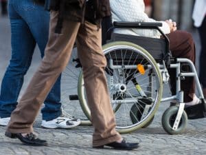 A travelling companion walking with a client in a wheelchair through a busy crowd, offering support and guidance.