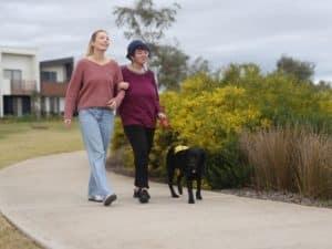 A visually impaired woman with a guide dog walks with a companion, highlighting pain assessment and disability support services.