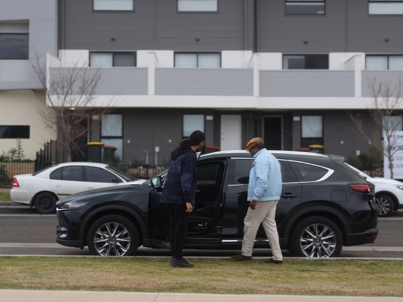 A black SUV parked in a residential area, with two men assessing its suitability for transport services for disabled people.