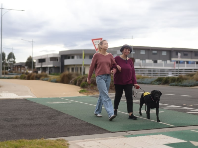 Two women walking a dog, enjoying inclusive activities in a park, promoting community engagement and outdoor fun.