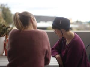 Support worker and person in conversation during a daily living skills assessment on a balcony, discussing independence and care needs.