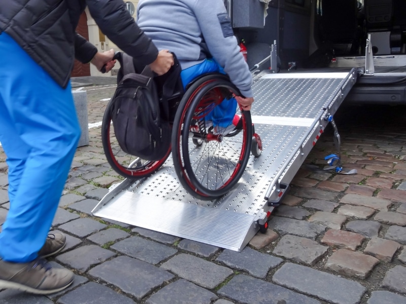 Wheelchair user receiving assistance with transportation using a fold-out ramp on a vehicle