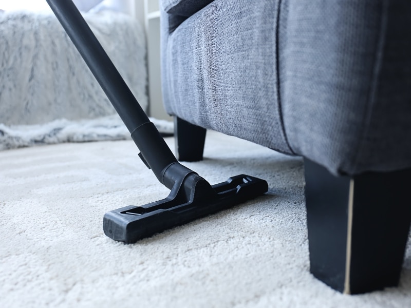 Vacuum nozzle cleaning dirty carpet near a grey lounge chair