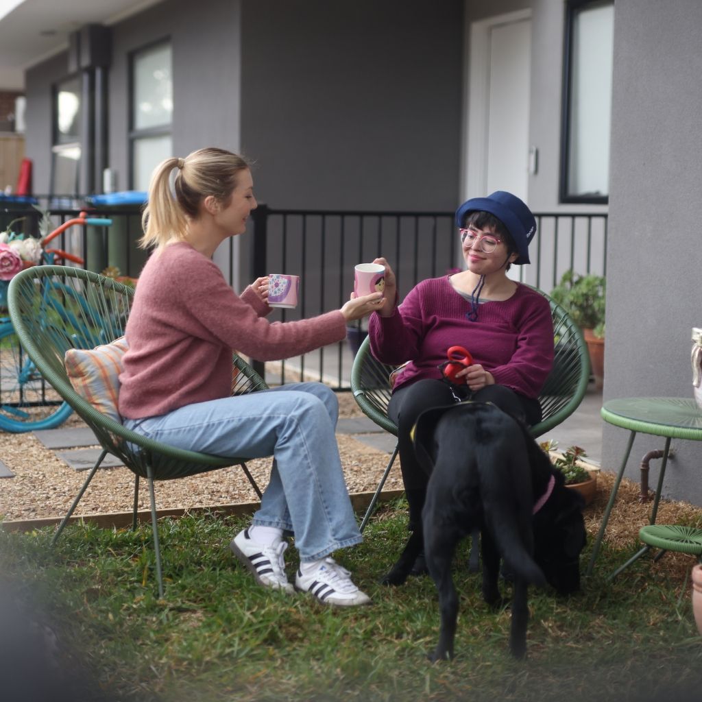 Support worker chatting with an NDIS participant outdoors beside a black dog