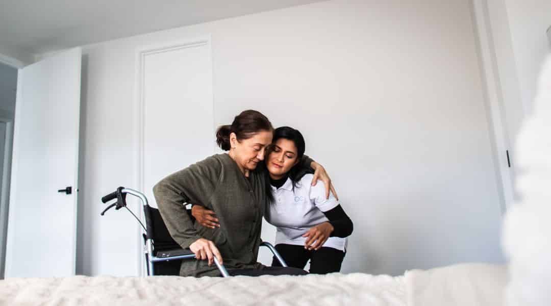 NDIS nurse supporting an older woman using a walker in her bedroom